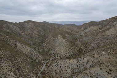 Almerya 'daki Tabernas Çölü' nün kurak manzarası (İspanya), dağlık bir manzara, çalılar var ve gökyüzü bulutlu.
