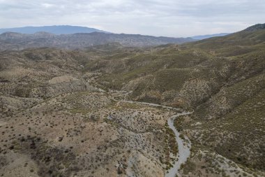 Almerya 'daki Tabernas Çölü' nün kurak manzarası (İspanya), dağlık bir manzara, çalılar var ve gökyüzü bulutlu.