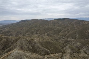 Almerya 'daki Tabernas Çölü' nün kurak manzarası (İspanya), dağlık bir manzara, çalılar var ve gökyüzü bulutlu.