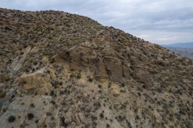 Almerya 'daki Tabernas Çölü' nün kurak manzarası (İspanya), dağlık bir manzara, çalılar var ve gökyüzü bulutlu.