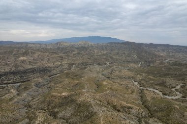 Almerya 'daki Tabernas Çölü' nün kurak manzarası (İspanya), dağlık bir manzara, çalılar var ve gökyüzü bulutlu.