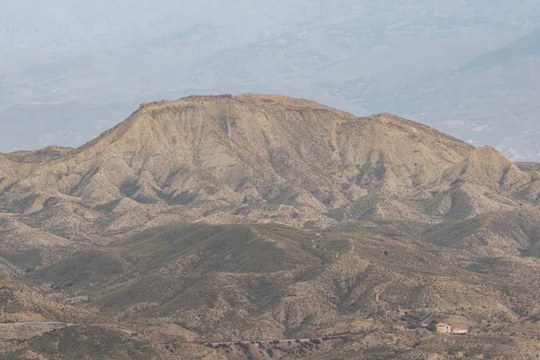 Almerya 'daki Tabernas Çölü' nün kurak manzarası (İspanya), dağlık bir manzaradır, birkaç ev, çalılıklar ve gökyüzü bulutludur.