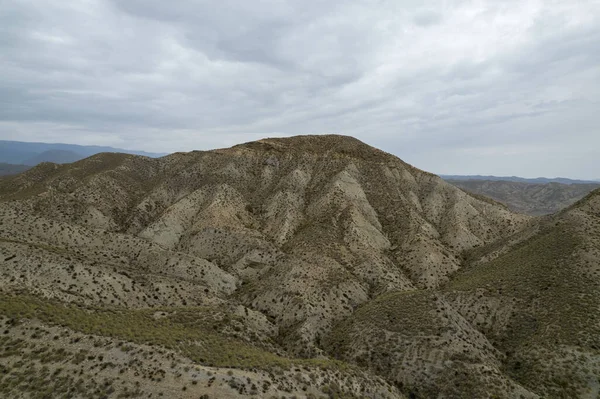 Almerya 'daki Tabernas Çölü' nün kurak manzarası (İspanya), dağlık bir manzara, çalılar var ve gökyüzü bulutlu.