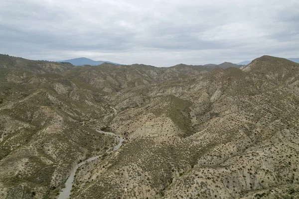 Almerya 'daki Tabernas Çölü' nün kurak manzarası (İspanya), dağlık bir manzara, çalılar var ve gökyüzü bulutlu.