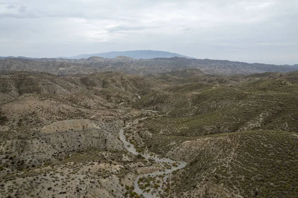 Almerya 'daki Tabernas Çölü' nün kurak manzarası (İspanya), dağlık bir manzara, çalılar var ve gökyüzü bulutlu.