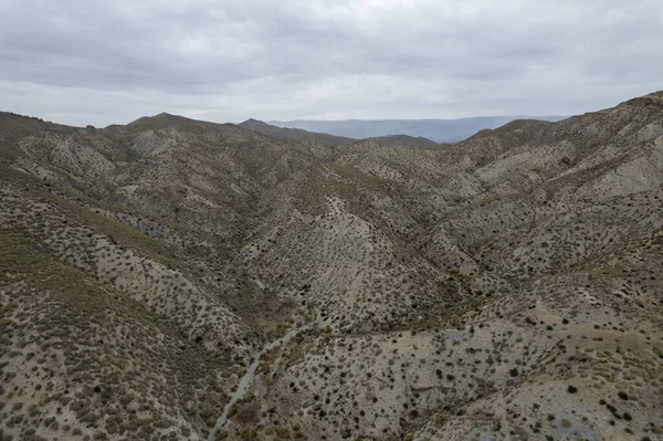 Almerya 'daki Tabernas Çölü' nün kurak manzarası (İspanya), dağlık bir manzara, çalılar var ve gökyüzü bulutlu.
