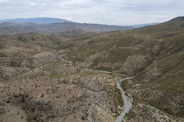 Almerya 'daki Tabernas Çölü' nün kurak manzarası (İspanya), dağlık bir manzara, çalılar var ve gökyüzü bulutlu.