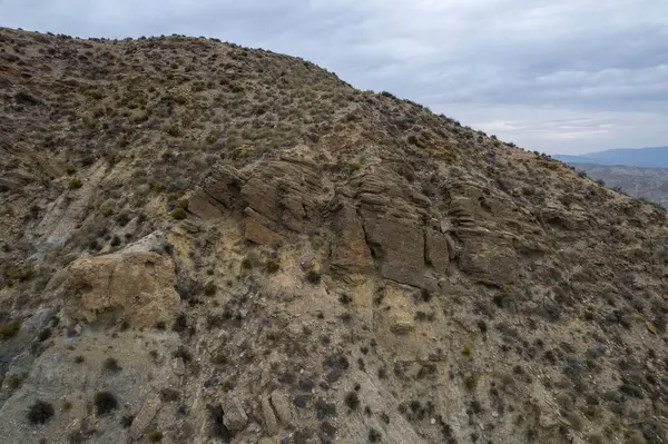 Almerya 'daki Tabernas Çölü' nün kurak manzarası (İspanya), dağlık bir manzara, çalılar var ve gökyüzü bulutlu.