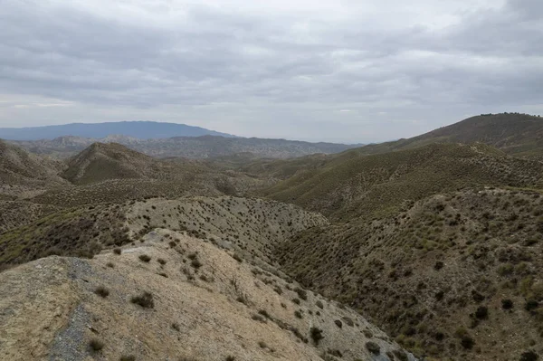 Almerya 'daki Tabernas Çölü' nün kurak manzarası (İspanya), dağlık bir manzara, çalılar var ve gökyüzü bulutlu.