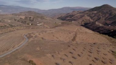 İspanya, Granada 'nın güneyindeki dağlık arazide badem ağaçları, dağ yamacında çalılar, çiftlik evleri, gökyüzünde bulutlar var.