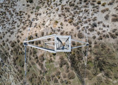 Yüksek voltajlı bir sütunun yukarıdaki fotoğrafı, kolon metalden yapılmış, kolon çalılarla dolu kurak bir alanda.