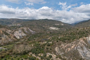Endülüs 'ün güneyindeki dağlık bölgede ağaçlar ve çalılar var, vadide birkaç çiftlik evi var, vadiler var, gökyüzü bulutlu.
