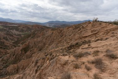 Endülüs 'ün güneyindeki dağlık bölgede çalılar, vadiler ve kurak bir bölge var. Gökyüzünde bulutlar var.