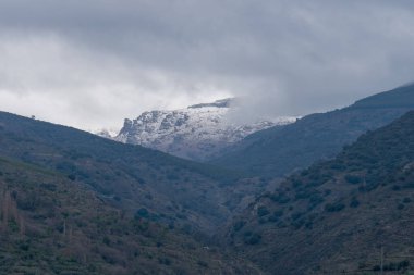 Sierra Nevada 'daki dağlık bölge, meşe ve çam ormanları, vadiler, kar, gökyüzü bulutlu.