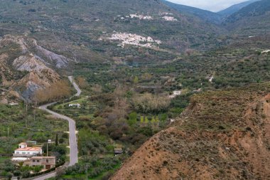 Güney Endülüs 'ün dağlık bölgesi, ağaçlar ve çalılar var, vadide birkaç çiftlik evi var, yamaçta birkaç köy var.