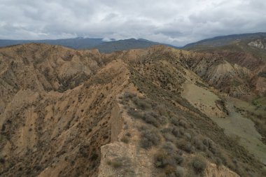 Endülüs 'ün güneyindeki dağlık bölgede çalılar, vadiler ve kurak bir bölge var. Gökyüzünde bulutlar var.