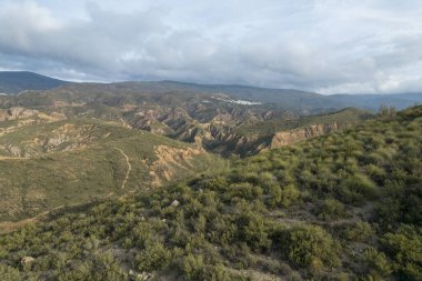 Güney Endülüs 'ün dağlık bölgesi, ağaçlar ve çalılar var, vadiler var, dağın yamacında bir köy var, gökyüzü bulutlu