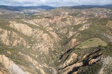 mountainous area of southern Andalusia, there are trees and bushes, there are ravines, there is a village on the side of the mountain, the sky is cloudy