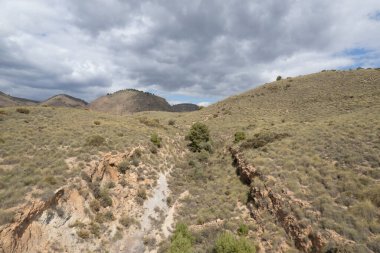 İspanya 'nın güneyindeki dağlık arazide çalılar, ağaçlar, gökyüzünde bulutlar var.