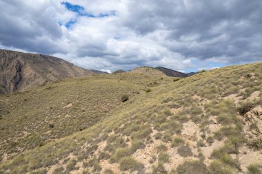 İspanya 'nın güneyindeki dağlık arazide çalılar, ağaçlar, gökyüzünde bulutlar var.
