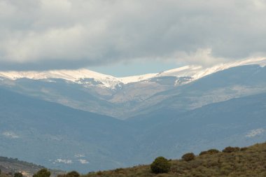 İspanya 'nın güneyindeki Sierra Nevada' nın dağlık arazisi, dağlarda kar var, ormanlar var, gökyüzü bulutlu.
