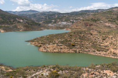 İspanya 'nın güneyindeki Beninar Barajı, dağlık bir bölge, ağaçlar ve çalılar var, gökyüzünde bulutlar var.