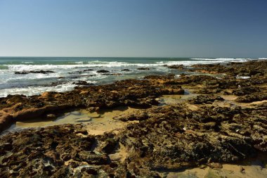 Bahçe Yolu 'ndaki Jeffreys Koyu' nda dalgalar çekildiğinde, arka planda açık mavi bir okyanus olan kayalar yükseliyor.