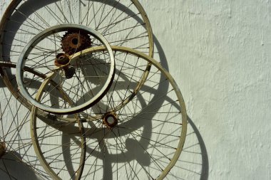 Eski paslı bisiklet jantları sert, beyaz bir duvara karşı dizilmişti.
