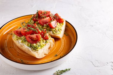 Büyük bir portakal tabağında avokado ve domatesli vejetaryen sandviçlerle kahvaltı, sağlıklı beslenme kavramı.