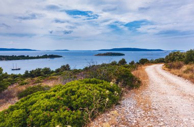 Hırvatistan. Adriyatik Körfezi 'nin Ciovo adasındaki manzarası. Denizdeki alışveriş merkezi adaları. Adadaki toprak yol boyunca çalılar ve dikenler..