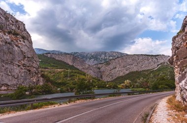 Hırvatistan. Cetina nehri boyunca uzanan yol ve Omis kasabasının çıkışındaki dağlar. Beyaz bulutlu mavi gökyüzü. Boşluğu kopyala.