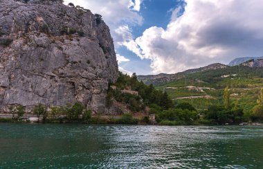 Hırvatistan. Cetina nehri ve kıyıdaki dağlar. Beyaz bulutlu mavi gökyüzü. Arka plan bulanık..