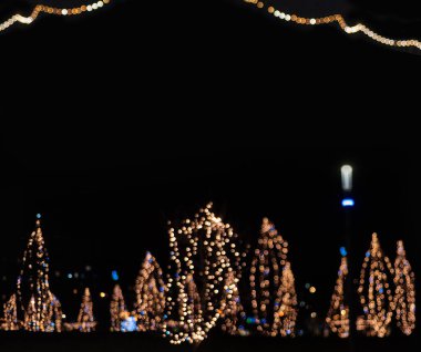 Bokeh for a festive New Year and Christmas background. Defocused abstract beige, yellow, white and blue light circles. Dark Christmas background. Garlands in the trees. Copy space.