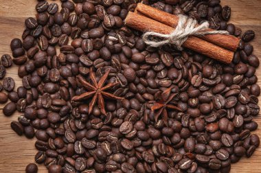 Kahve çekirdekleri, iki tarçın çubuğu ve iki anason yıldızı ahşap masaya saçılmış..