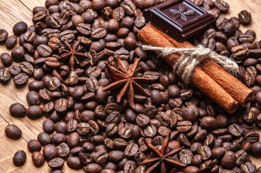 Kahve çekirdekleri, iki tarçın çubuğu, bir parça çikolata ve iki anason yıldızı ahşap masaya saçıldı. Boşluğu kopyala.