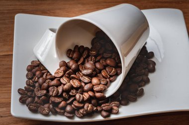 Kahve çekirdekleri fincandan çay tabağına dökülür. Gövde ahşap bir masanın üzerinde. Boşluğu kopyala..