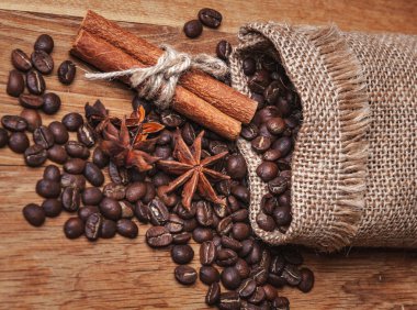 Kahve çekirdekleri torbadan ahşap masaya döküldü. Tahılların arasında anason yıldızları ve tarçın çubukları var. Boşluğu kopyala..