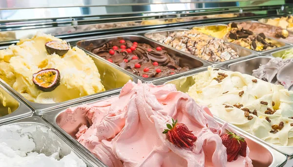 Multi colored Italian ice cream gelato with various fruit flavors decorated with fruits, nuts or chocolate  in the refrigerator-display case. Ice cream trays.Italian cuisine. Gourmet dessert.