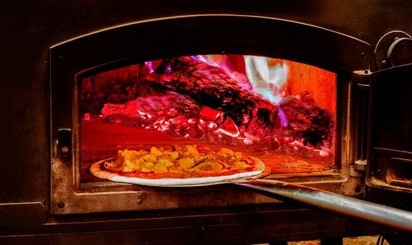 Wood-fired pizza oven. Close-up of a pizza direct putting in to bake in a red-hot wood-fired pizza oven. Gourmet meal. Italian cuisine.