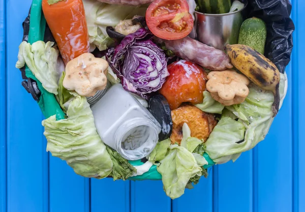 Waste bin with unused food. Food waste as a global problem in the world. Isolated on a light blue background as a symbol of the fight against global warming and environmental pollution. Copy space.  Food waste concept.