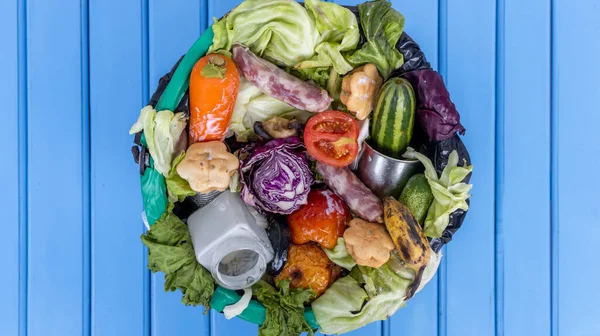 Waste bin with unused food. Food waste as a global problem in the world. Isolated on a light blue background as a symbol of the fight against global warming and environmental pollution. Copy space.  Food waste concept.