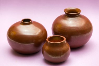 Kahverengi tonlarda, pembe arkaplana yerleştirilmiş üç seramik tencereyle durgun bir hayat