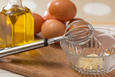 Bir mutfak tahtasına yerleştirilmiş yumurta ve yağlı bir hayat, bir çırpıcı ve mayonez dolu bir kase.