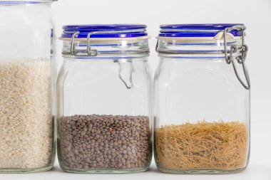 İçinde çiğ yemek, pirinç, mercimek ve ince erişte bulunan üç kiler kavanozu.