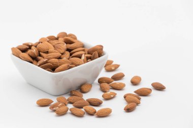 Beyaz arka planda soyulmuş bademlerin olduğu kare bir kasenin görüntüsü, kaseden birkaç badem düştü.