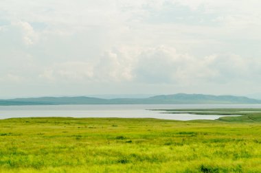 Güzel bozkır manzarası: arka planda çayır, göl, dağlar ve bulutlar.