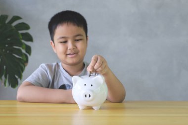 Asyalı çocuk Piggy Bank 'a iyi para koymalar. Para biriktirme kavramı.