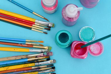 Mavi arka planda kullanılmış fırça ve boya kapları grubu.