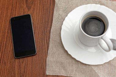 Bir fincan kahve ve cep telefonu ahşap masada..