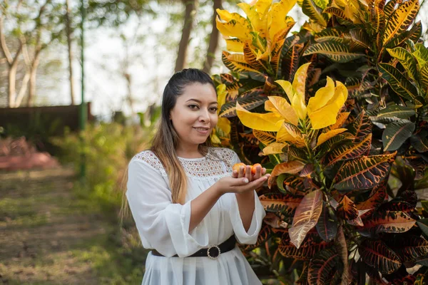 Portrait of young woman next to garden plant. Portrait of Mexican woman in a garden next to colorful croton plant. Codiaeum variegatum.